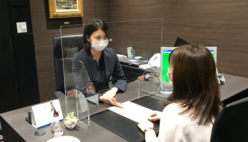 (写真)アクリルパネルをはさんで接客する支店の窓口担当者